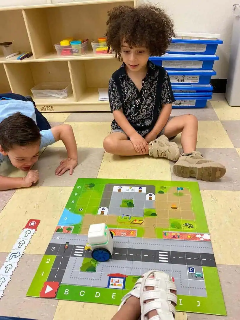 Niños programando un robot sobre un tablero de actividades en el piso