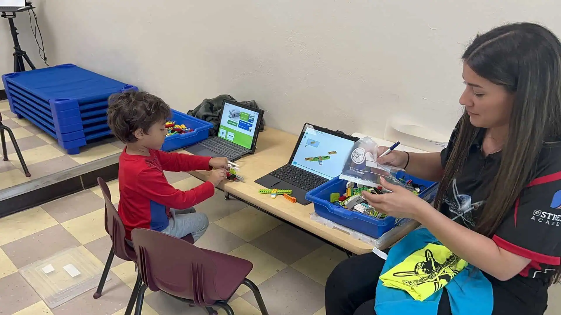 Maestra guiando a un estudiante en actividad de robótica con laptop
